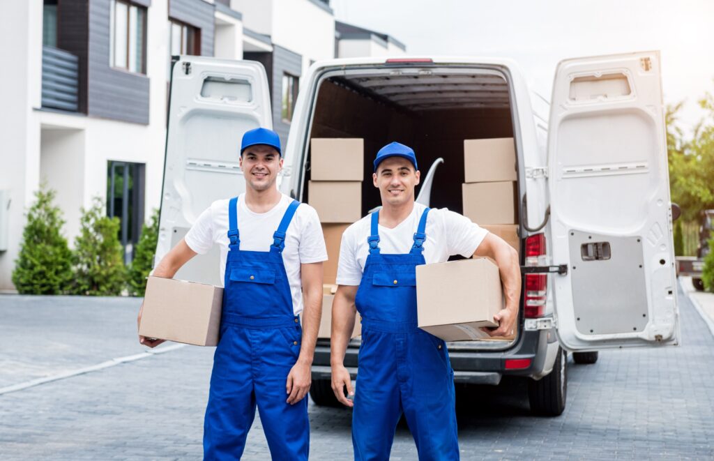 Benefits of Hiring a Moving Company -Two smiling movers holding boxes in front of a moving van