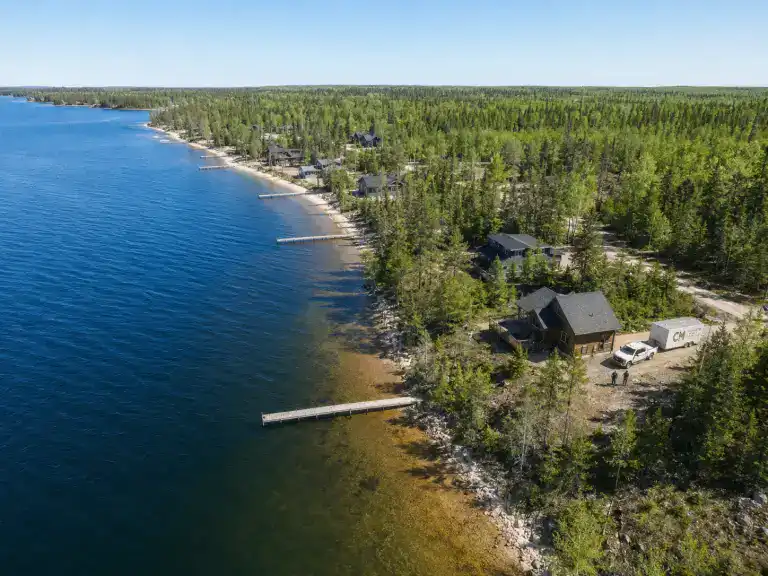 Aerial view of Lake Winnipeg east shore with a row of wooden cabins along the shoreline, pine trees, and clear blue water in summer, Grand Beach area Manitoba