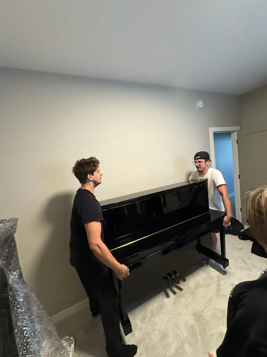 Piano movers in Winnipeg carrying a glossy black upright piano through a home